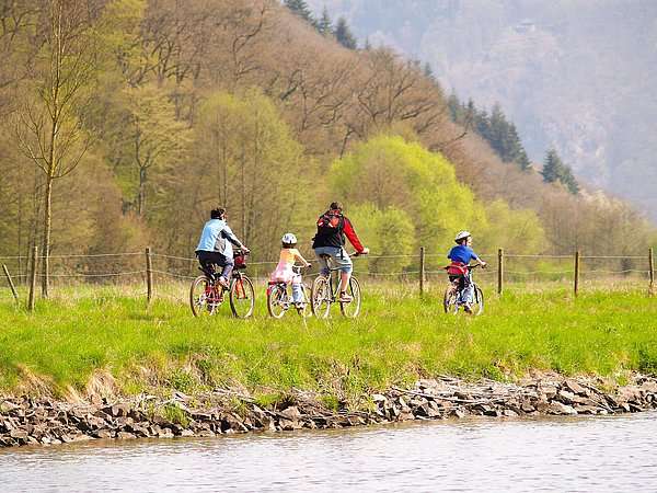 Ein Foto, auf dem eine Familie eine Fahrradtour im Grünen, am Wasser unternimmt.